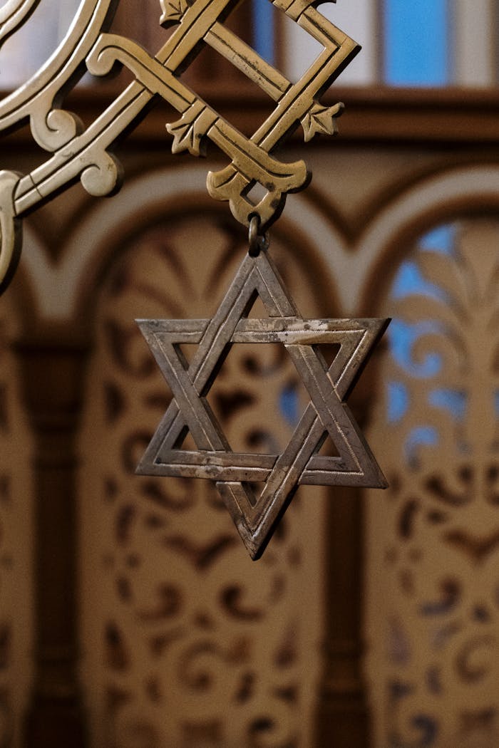 Intricate metal Star of David hanging inside a decorative architectural structure.