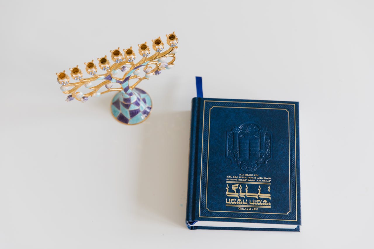 An ornate menorah and a Hebrew book on a white surface, perfect for Hanukkah themes.